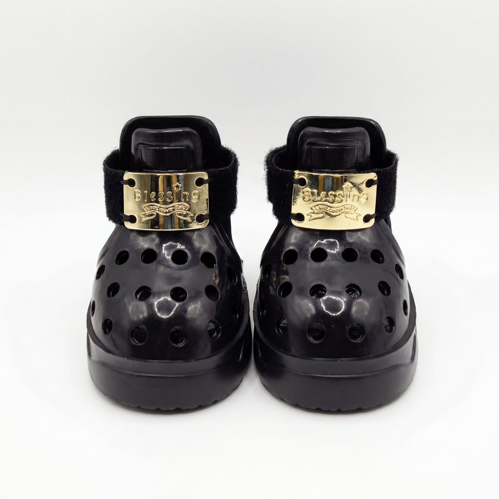 Front closeup view of a pair of Blessingmychild V1 classic black dog sandals highlighting the shiny front-engraved brand gold emblems